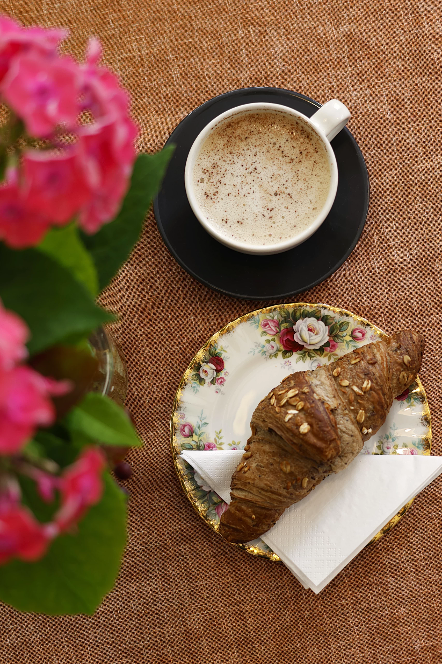 Kauralatte ja vegaaninen croissant kukkien kera Encanto Art Cafessa